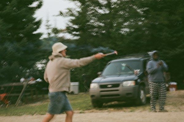 A person in a bucket hat pointing something across a campsite
