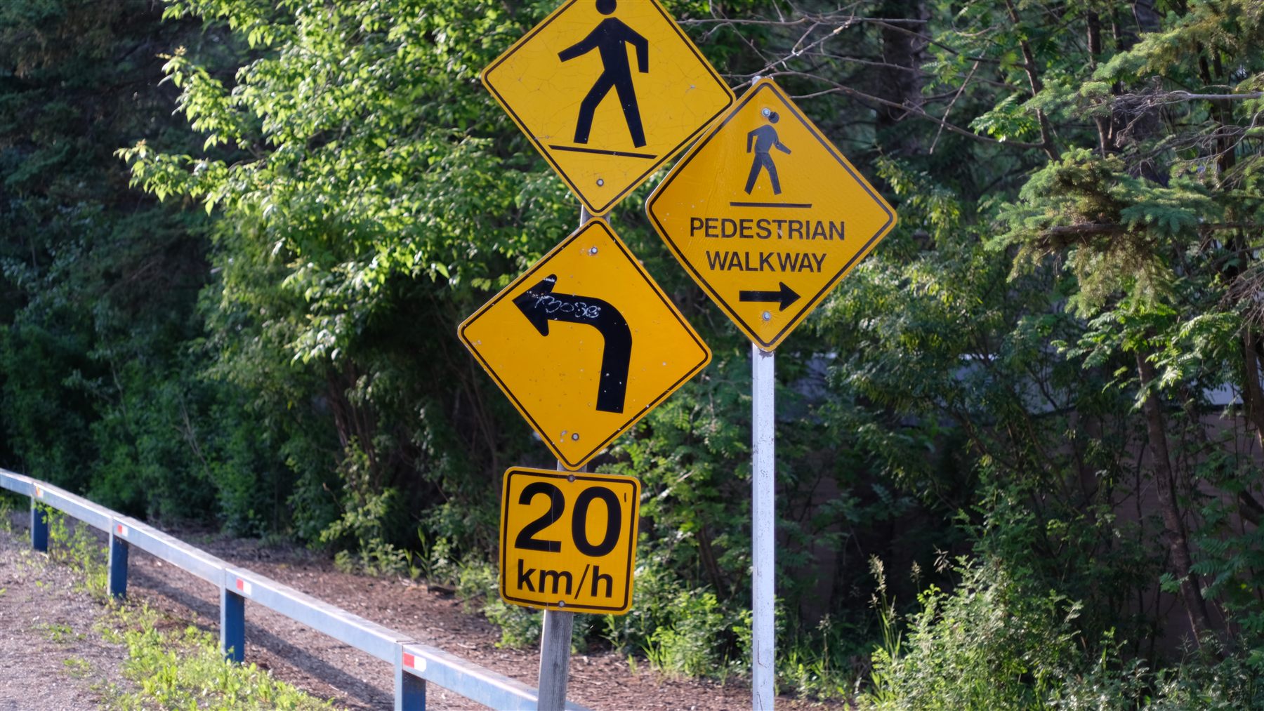 Yellow road signs beside a guardrail